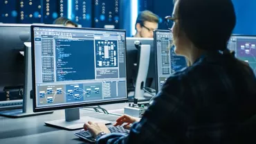 Person working at a desk with computer screens displaying code and diagrams.