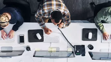 Overhead view of three people working at computers in an office.