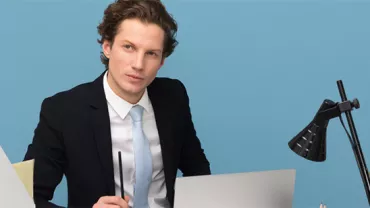 Professional sitting at a desk with a laptop and lamp.