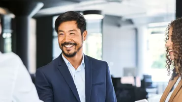 A man in a work suit smiling to a woman in white while another listens in