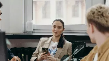 Three people having a conversation in an office setting, one holding a phone.