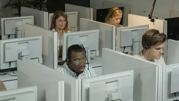 People working at individual cubicles with computers.