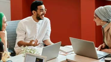 Group of professionals discussing at a table with laptops.