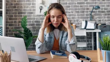 Woman at desk looking stressed with laptop and headphones.