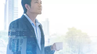 A person in a suit holding a coffee cup with a cityscape blended in the background.