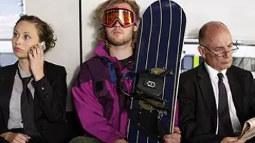 Three people on public transport, one holding a snowboard.