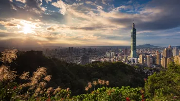 Wide cityscape of Taipei 101 against a sunset skyline.