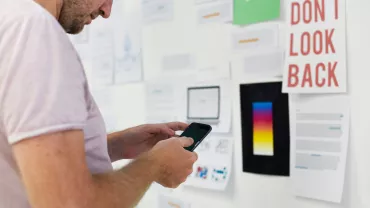 A person using a smartphone while examining notes on a wall.