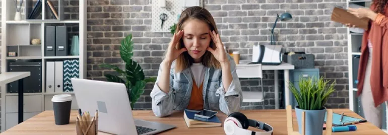 Woman at desk looking stressed with laptop and headphones.